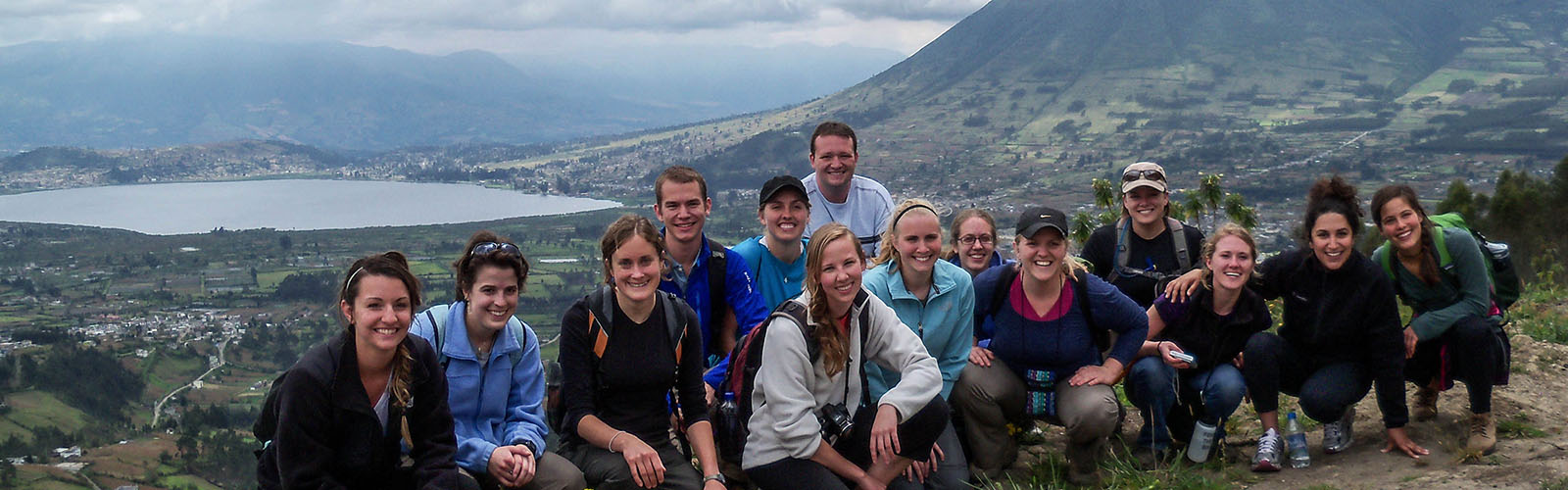 Students are gathered together in front of the mountains. They are in outdoor gear and smiling at the camera.